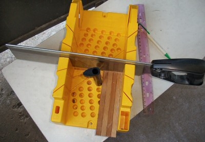 Using a miter-box, we align multiple cut beams and secure them with the retaining pin under tension, and miter-cut the ends square. Turning the beams around and measuring for correct length, we again cut-off the ends.